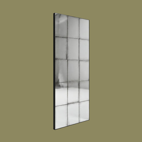 Tall rectangular antiqued panel wall mirror with black metal grid detailing and distressed vintage-style glass against a muted olive background.