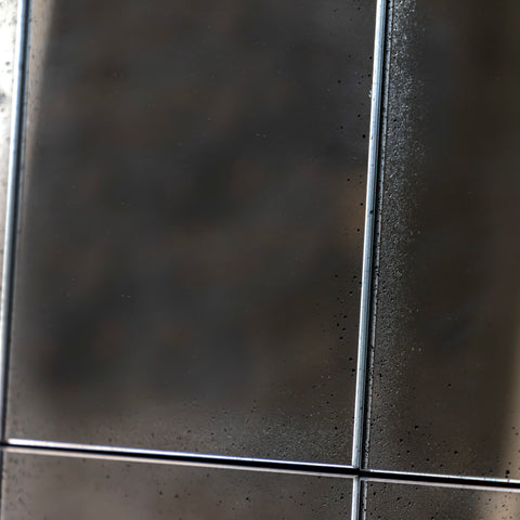 Close-up of a distressed windowpane mirror featuring textured antiqued glass and dark metal framing.