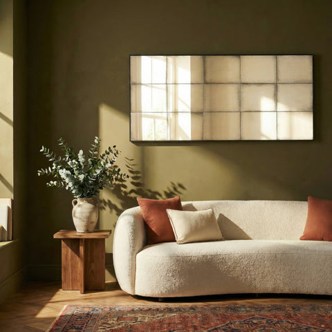 Contemporary rectangular grid mirror above a textured cream sofa with warm sunlight and earthy decor.