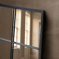 Close-up detail of a black metal grid wall mirror with industrial windowpane styling and warm natural light reflections.