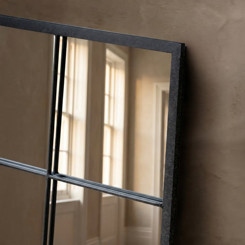 Close-up detail of a black metal grid wall mirror with industrial windowpane styling and warm natural light reflections.