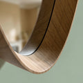 Minimalist wooden oval mirror detail with soft natural lighting and neutral interior background.