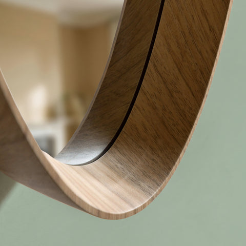 Minimalist wooden oval mirror detail with soft natural lighting and neutral interior background.