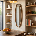 Minimalist oval mirror with wood trim in a bright kitchen space featuring open shelving and earthy tones