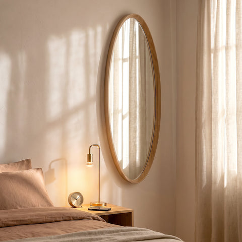 Modern oval mirror with natural wood frame in a serene neutral bedroom interior.