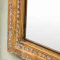 Macro shot of an ornate gold mirror frame highlighting textured carved detailing, delicate beading and aged metallic accents.