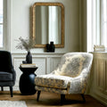 Gold-framed decorative wall mirror with intricate carved detailing, styled in a refined room setting with soft natural light and elegant furnishings.