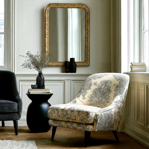 Gold-framed decorative wall mirror with intricate carved detailing, styled in a refined room setting with soft natural light and elegant furnishings.