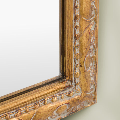 Detailed close-up of a decorative gold mirror frame showcasing embossed scroll detailing, beaded edging and vintage-inspired character.