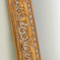 Close-up detail of an ornate gold mirror frame featuring intricate carved scrollwork, raised beading and antique-inspired texture.
