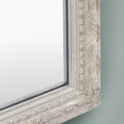 Close-up detail of a distressed cream mirror frame featuring ornate carved detailing, subtle speckled texture, raised beading and antique-inspired edging.