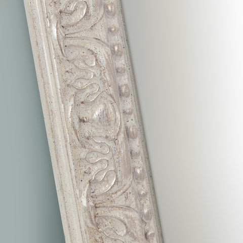 Decorative mirror frame detail with a distressed cream finish, refined carved pattern, raised beading and antique-style accents.