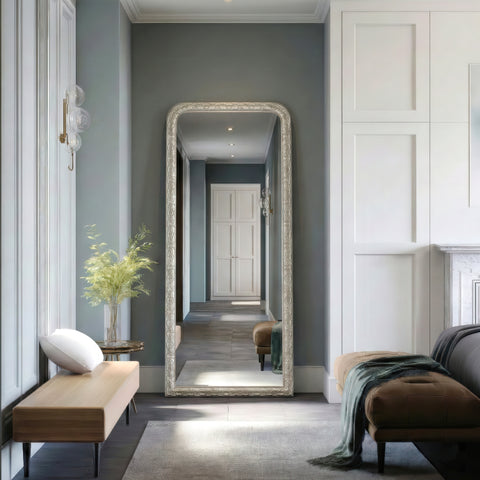 Traditional silver leaner mirror featuring intricate carved detailing, positioned in an elegant room creating a hallway setting to enhance light and depth.
