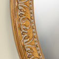 Detailed close-up of a decorative gold mirror frame showcasing embossed scroll detailing, beaded edging and vintage-inspired character.