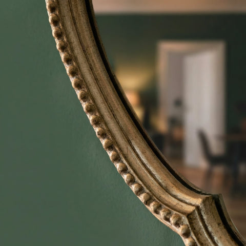 close up of a round scalloped wall mirror with ornate champagne gold frame and decorative beaded detailing